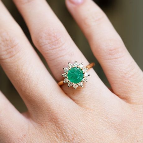 Emerald and diamond cluster ring close detail showing rich green tone and halo setting.