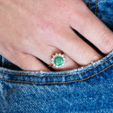 Emerald cluster ring worn with denim showing contrast of green stone and diamond cluster.