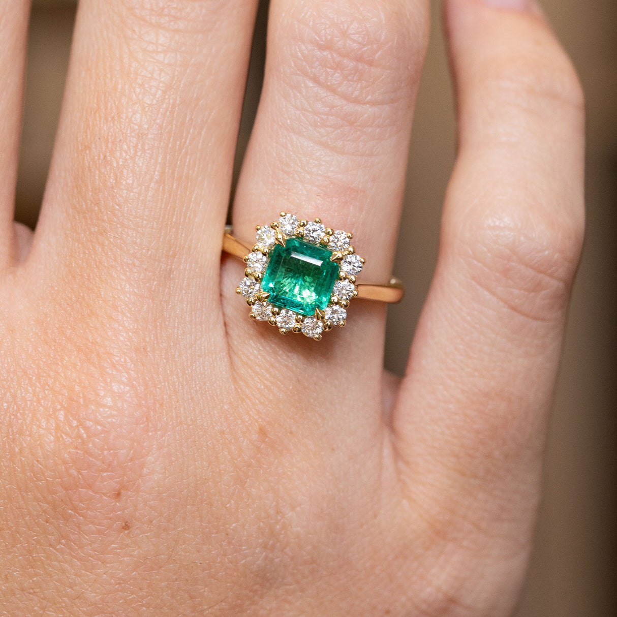 Antique-inspired emerald and diamond cluster engagement ring shown worn on the hand, featuring an emerald-cut emerald and diamond halo.