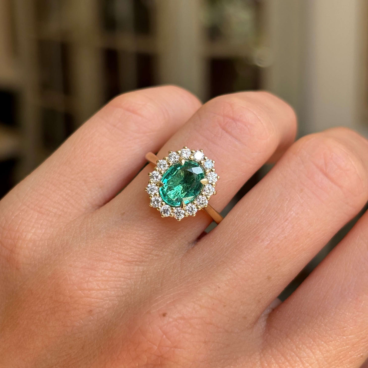 Antique-inspired oval emerald and diamond cluster ring in yellow gold displayed on hand, highlighting the rich green gemstone, sparkling diamonds and timeless design.