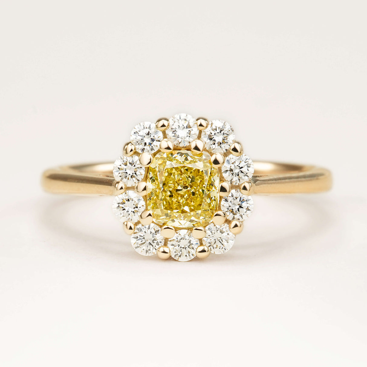 Fancy yellow cushion-cut yellow diamond cluster engagement ring in yellow gold.