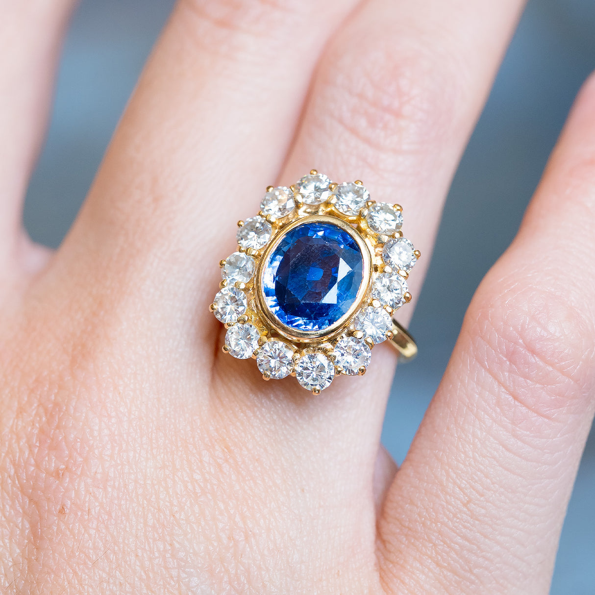 Vintage French sapphire and diamond cluster ring with vivid oval blue sapphire framed by brilliant-cut diamonds.