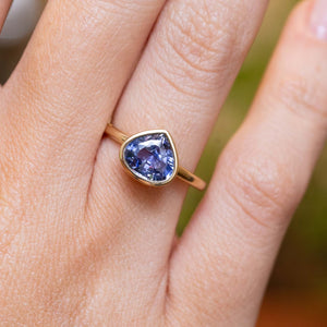 An antique-inspired pear-cut blue sapphire solitaire engagement ring in yellow gold worn on the finger.