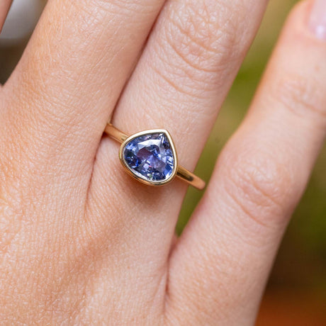 An antique-inspired pear-cut blue sapphire solitaire engagement ring in yellow gold worn on the finger.