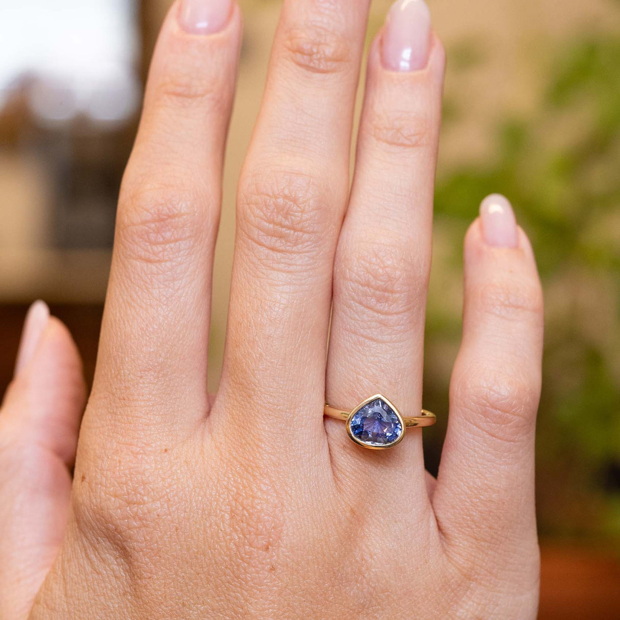 Pear-cut blue sapphire solitaire ring in yellow gold displayed on the hand with an antique-inspired setting.