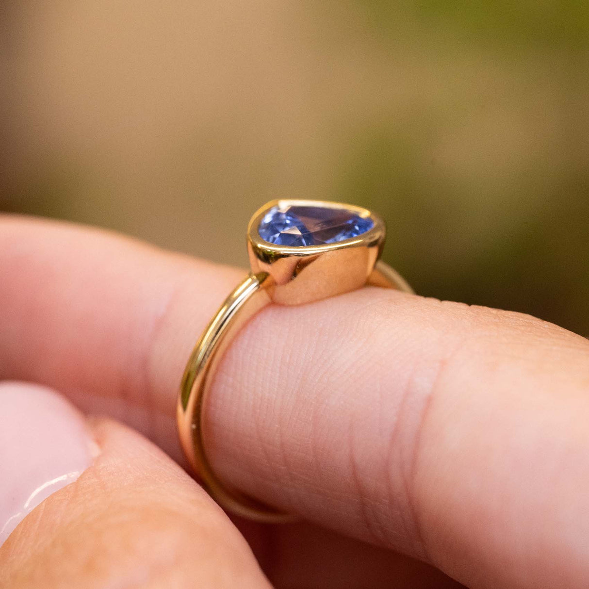 Gallery view showcasing the bezel setting of an antique-inspired pear-cut blue sapphire solitaire ring in yellow gold.