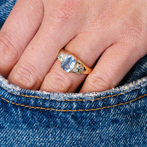 Close-up of a hand wearing a sapphire and diamond ring worn on hand with denim pocket detail.