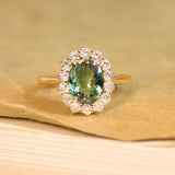 Green alexandrite and diamond cluster engagement ring featuring an oval alexandrite surrounded by a halo of brilliant-cut diamonds in yellow gold.
