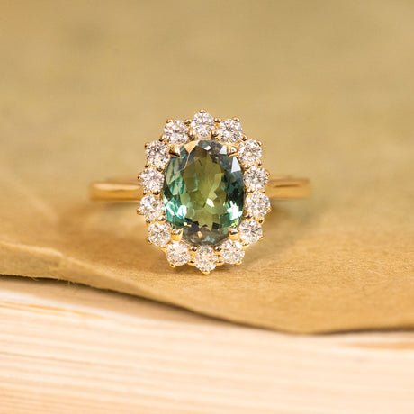 Green alexandrite and diamond cluster engagement ring featuring an oval alexandrite surrounded by a halo of brilliant-cut diamonds in yellow gold.