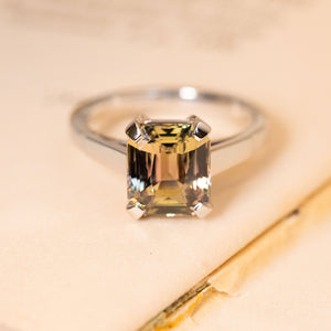 Green and brown colour-change sapphire solitaire engagement ring featuring an emerald-cut sapphire in a four-claw white gold setting.