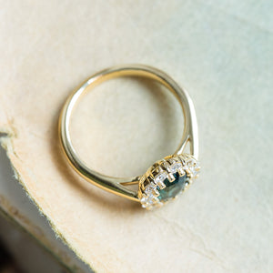 Green sapphire and diamond cluster engagement ring with elevated diamond halo and polished gold band.