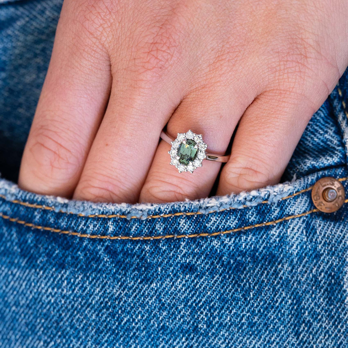 Green sapphire cluster ring worn on hand with denim pocket detail.