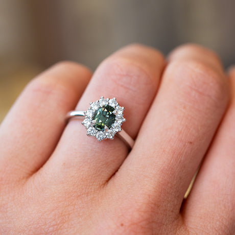 Close-up of a hand wearing a ring with a green sapphire and diamond halo.