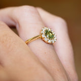 Green sapphire and diamond cluster engagement ring with raised setting and slim yellow gold band.