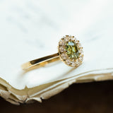 Green sapphire and diamond cluster engagement ring with yellow gold band and diamond halo.