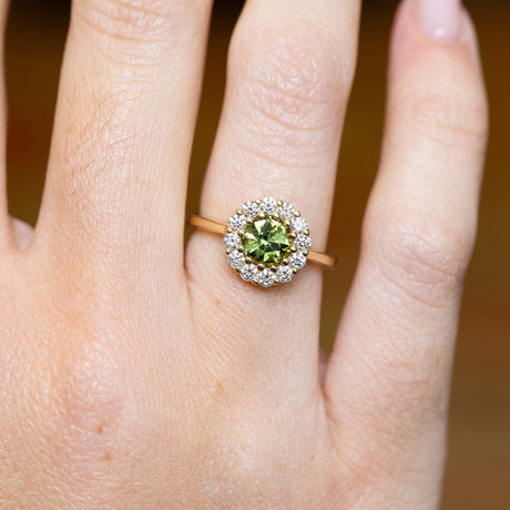 Green sapphire and diamond cluster engagement ring with round green sapphire and sparkling diamond halo.