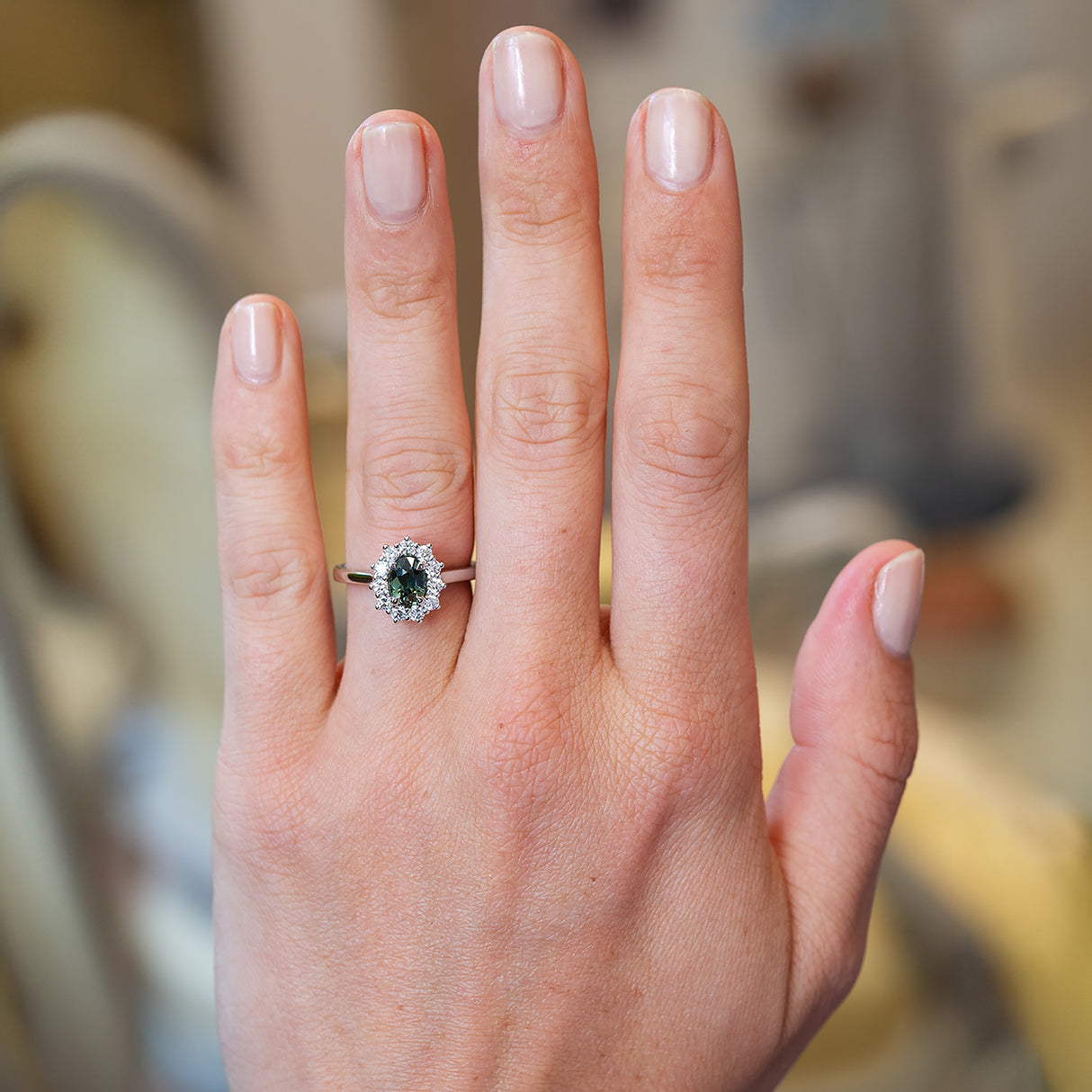 Green sapphire and diamond cluster ring worn on hand.