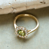 Green sapphire and diamond cluster engagement ring resting on textured paper background.