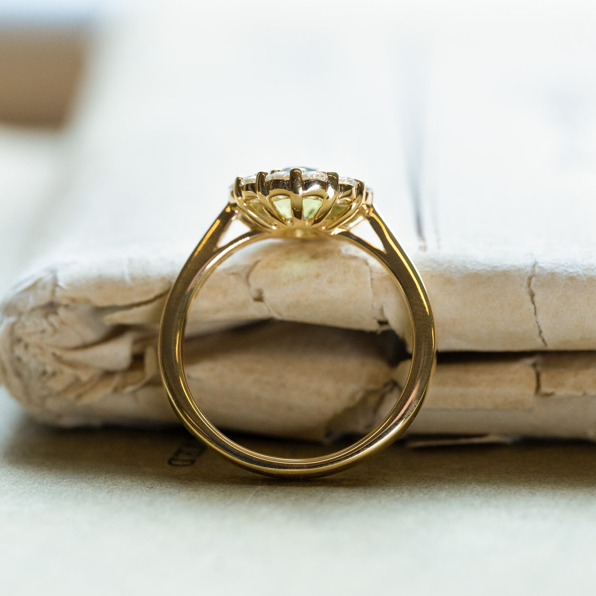 Green sapphire and diamond cluster engagement ring with raised basket setting and yellow gold band.
