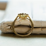 Green sapphire and diamond cluster engagement ring with raised basket setting and yellow gold band.