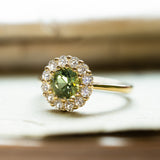 Green sapphire and diamond cluster engagement ring with round green sapphire and diamond surround.