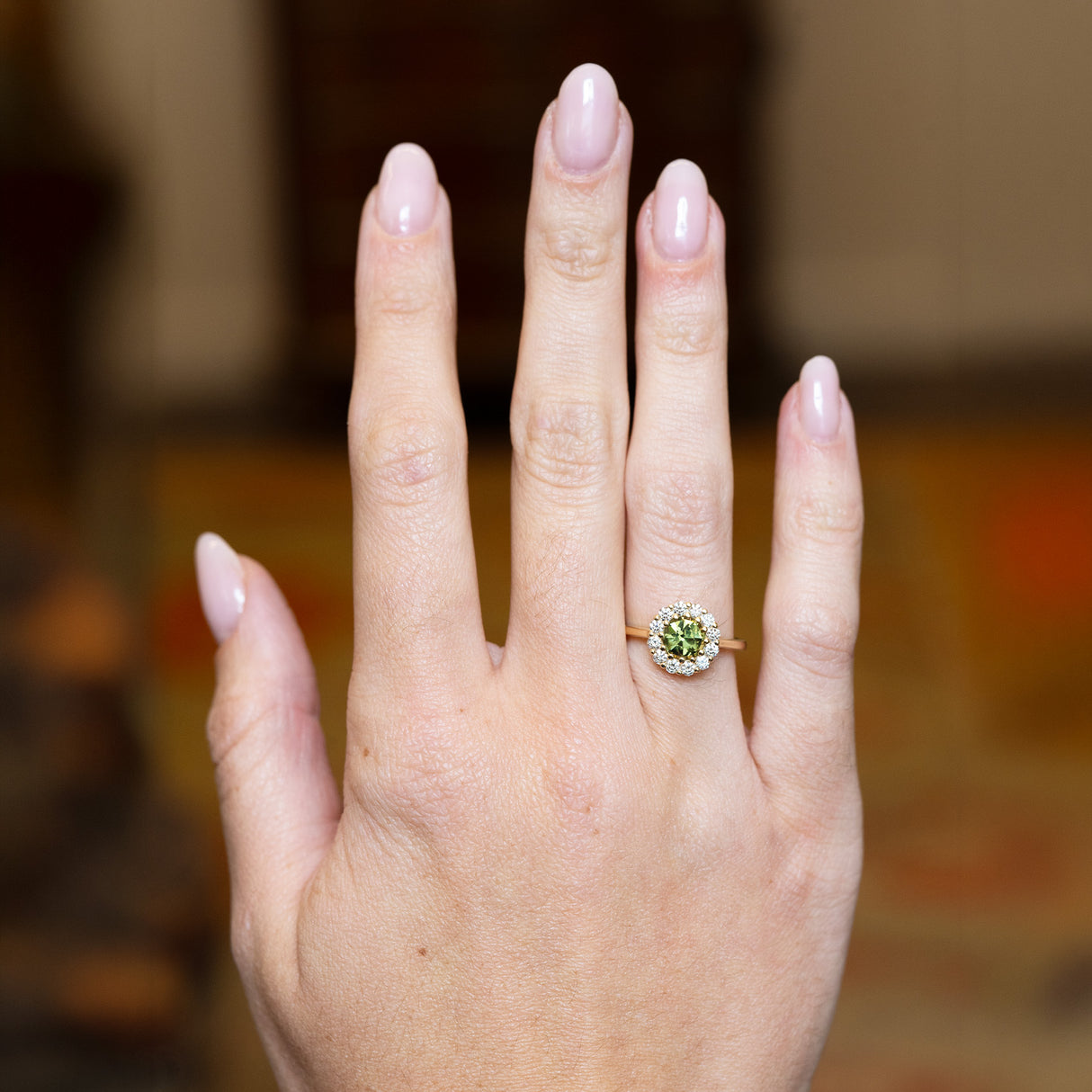 Green sapphire and diamond cluster engagement ring worn on hand with yellow gold band.