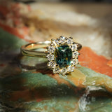 Green sapphire center stone with diamond cluster halo in gold band