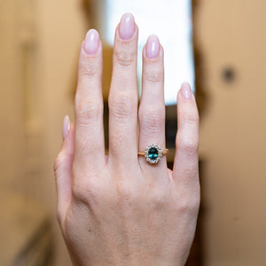 Antique inspired green sapphire and diamond cluster engagement ring worn on hand.