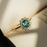 Oval green sapphire cluster ring with diamond halo in yellow gold on a book