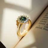 Green sapphire surrounded by diamond halo cluster engagement ring on a book