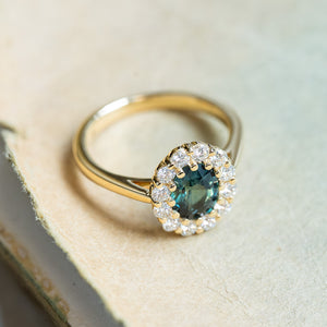 Antique inspired green sapphire and diamond cluster engagement ring resting on antique book pages.