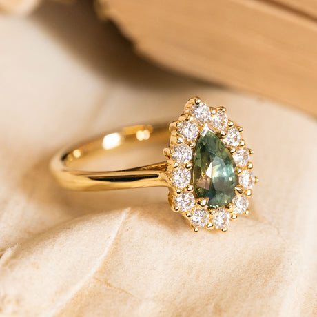 Pear-cut green sapphire and diamond cluster engagement ring with a vivid green sapphire framed by brilliant-cut diamonds in yellow gold.