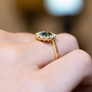 Antique inspired green sapphire and diamond cluster engagement ring with polished gold band and diamond halo.
