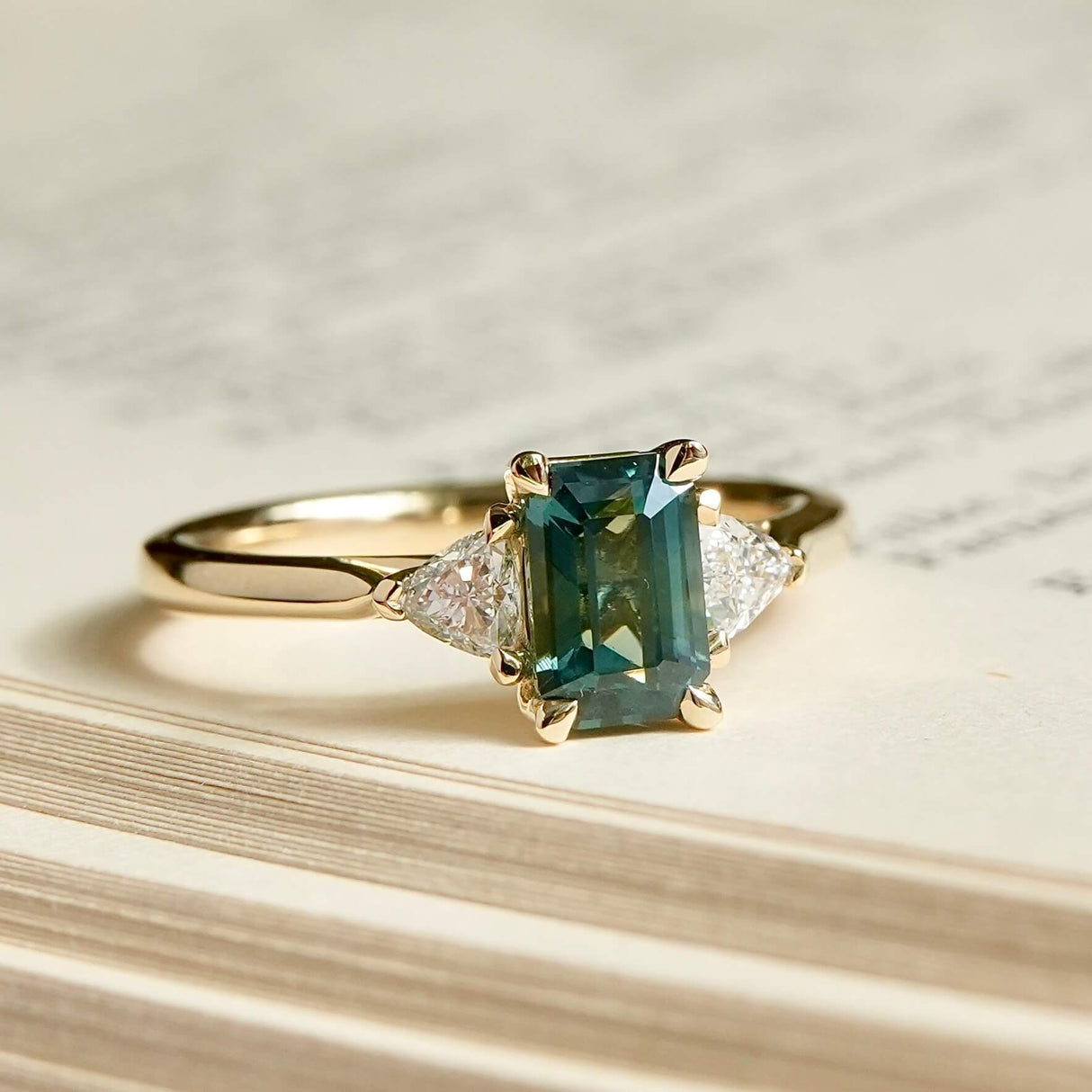 Emerald cut green sapphire engagement ring with diamond side stones in yellow gold