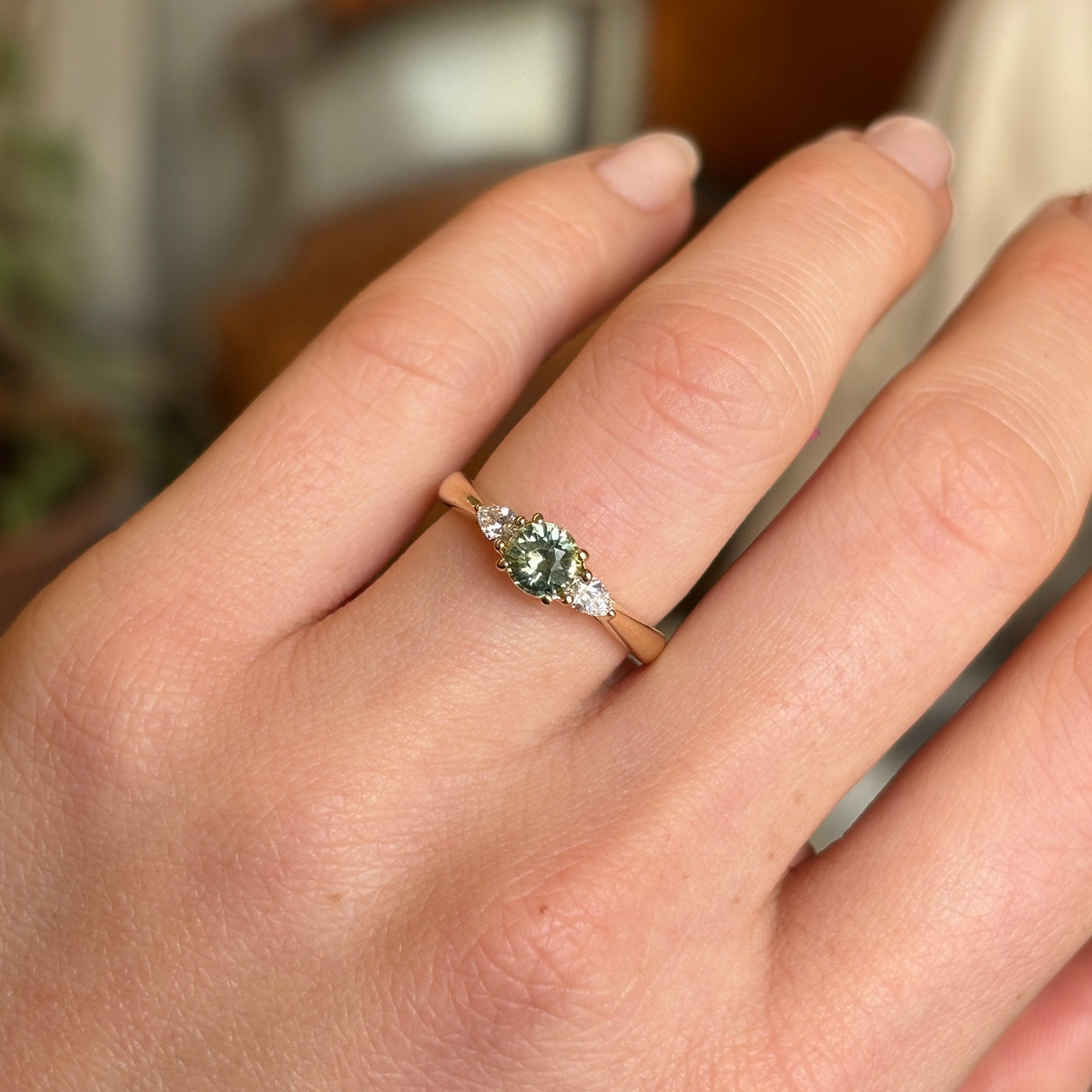 Round green sapphire and diamond three-stone engagement ring shown on hand in yellow gold setting.