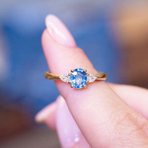 Light blue sapphire and diamond three-stone engagement ring with oval sapphire centre stone held between fingers.