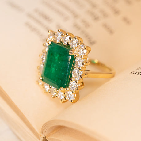 Statement emerald and diamond cocktail ring showcasing a 6.68ct emerald framed by a sparkling diamond cluster in yellow gold.