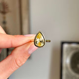 Antique-inspired large pear-cut Sri Lankan yellow sapphire in a smooth yellow gold rub-over setting, held between fingers against a softly blurred vintage interior background.