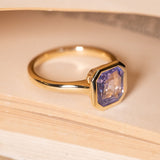 Antique-inspired lavender sapphire solitaire ring showcasing an emerald-cut lavender sapphire in a yellow gold rub-over setting.