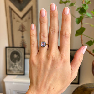 Antique-inspired yellow gold solitaire engagement ring worn on hand, featuring a square lavender sapphire in a sleek rub-over setting with soft lilac-blue tones.