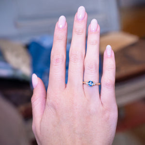 Light blue sapphire and diamond three-stone engagement ring worn on hand with gold band.