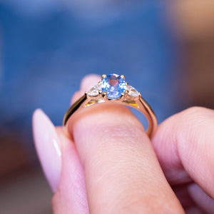 Light blue sapphire and diamond three-stone engagement ring held between fingers showing diamond detailing.