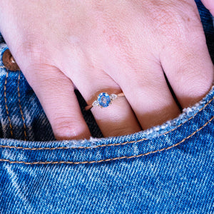 Light blue sapphire and diamond three-stone engagement ring worn on hand with denim pocket styling.