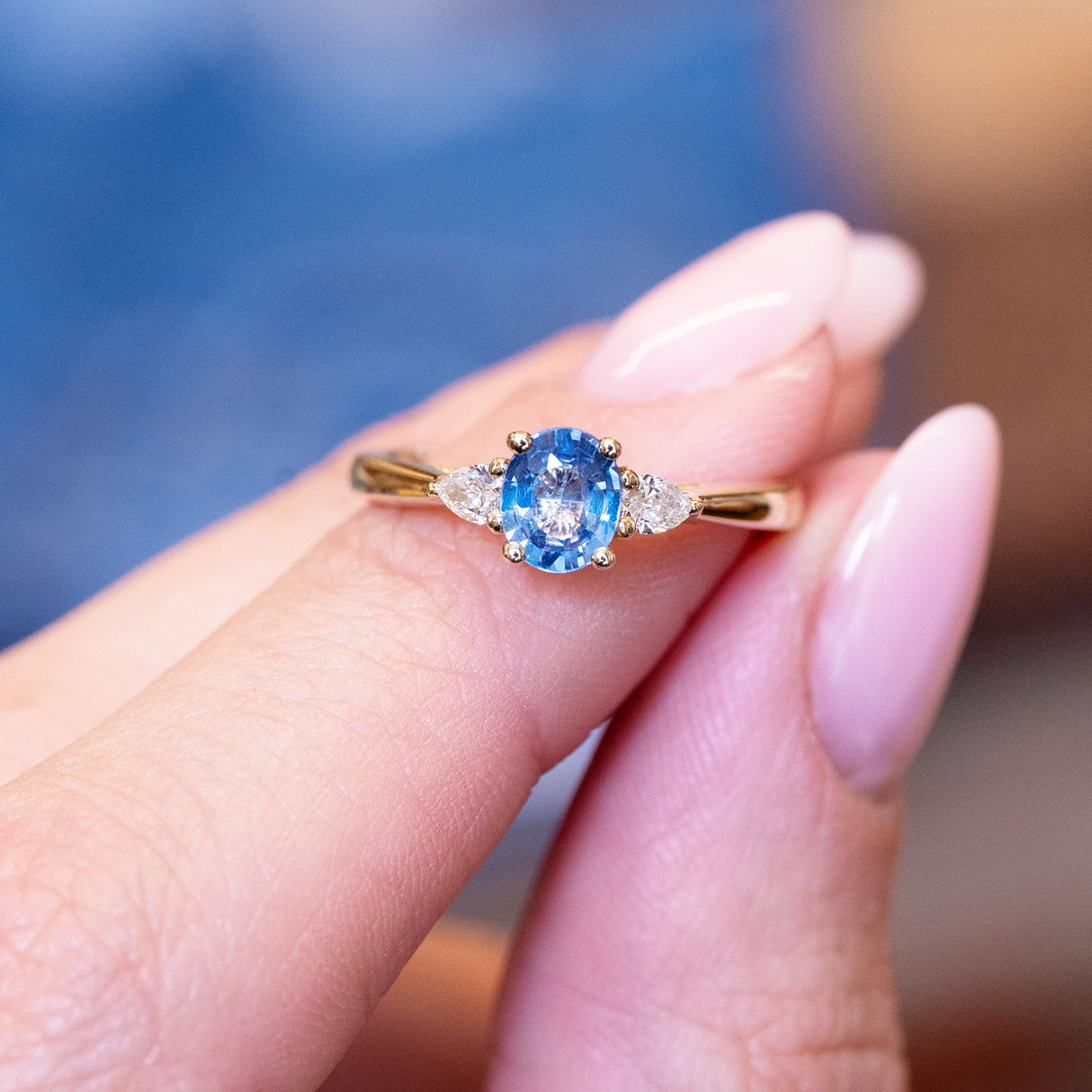 Light blue sapphire and diamond three-stone engagement ring with delicate diamond side stones and gold band.