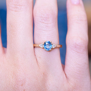 Light blue sapphire and diamond three-stone engagement ring with oval sapphire centre stone worn on finger.