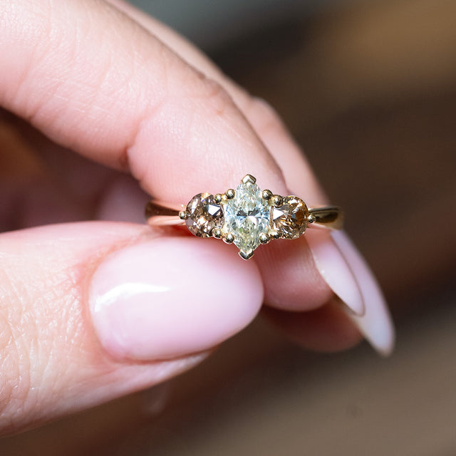 Diamond three-stone engagement ring with diamond accents held between fingers.