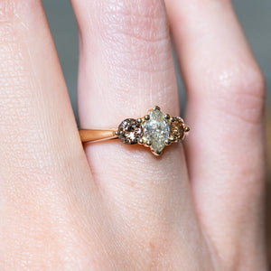 Diamond three-stone engagement ring with marquise-cut centre diamond and warm-toned side stones worn on hand.