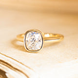 Cushion old-cut diamond solitaire engagement ring with a bezel-set diamond and polished yellow gold band.