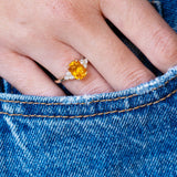 Close-up of a hand wearing a ring with an  orange sapphire, with a blue denim pocket detail.