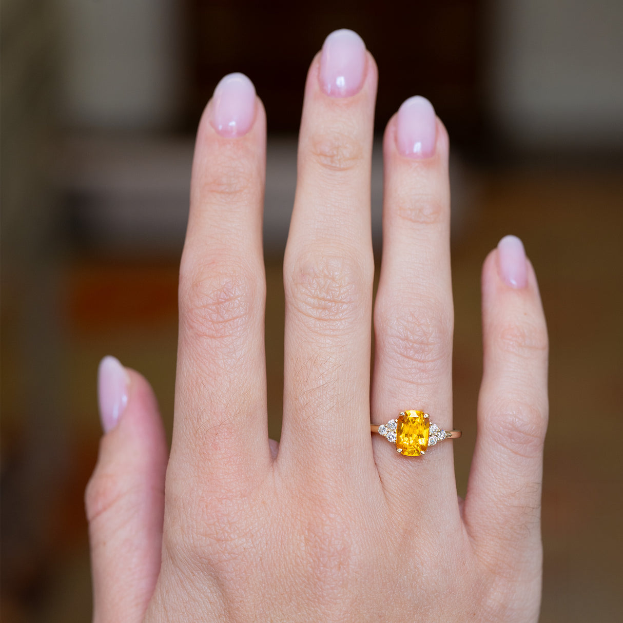 Hand wearing an orange cushion cut sapphire and diamond cluster trefoil ring.